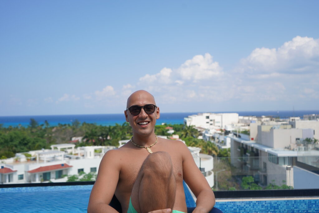 Yassine, founder of Habibi Yassine tour guide service, smiling by a pool with a scenic view of Playa del Carmen and the ocean in the background.