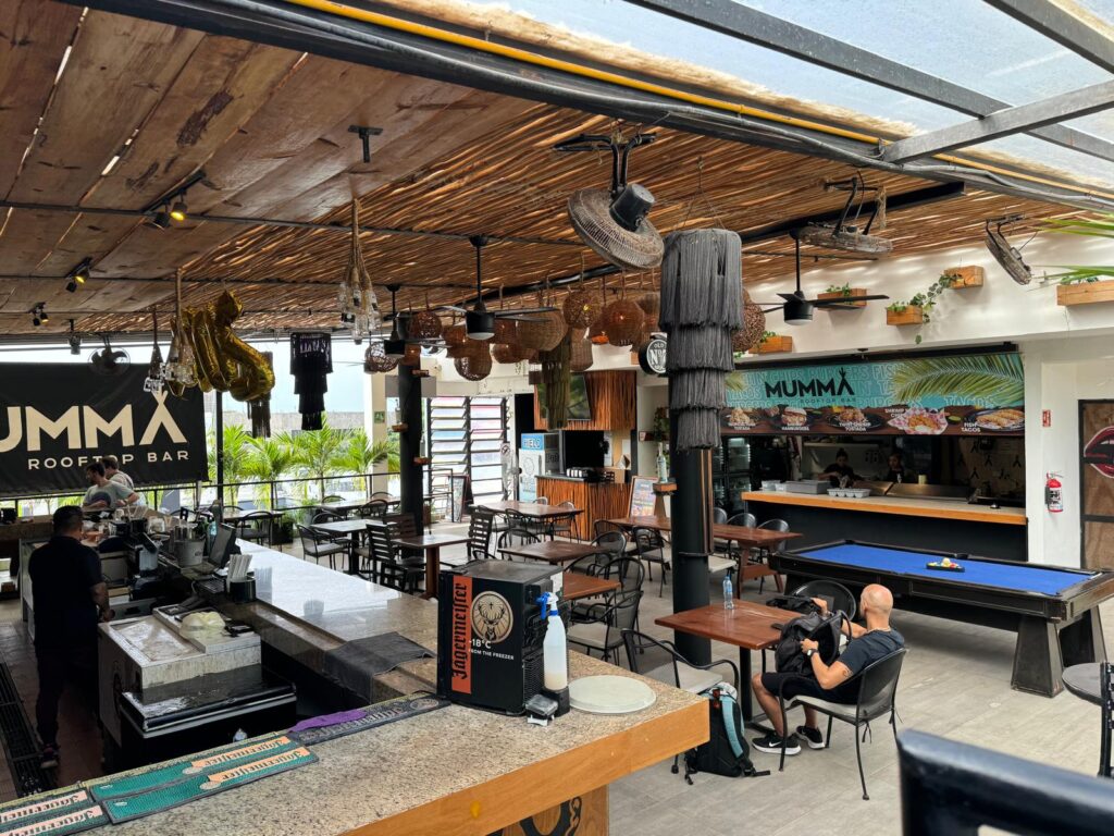 Interior of Mumma Rooftop Bar with a bar counter, seating area, pool table, and decorative hanging lights.