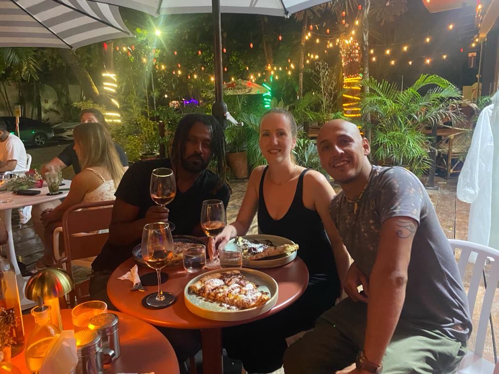 Yassine, founder of Habibi Yassine tour guide service, sitting at an outdoor restaurant table with two new friends, enjoying wine and pizza under string lights.